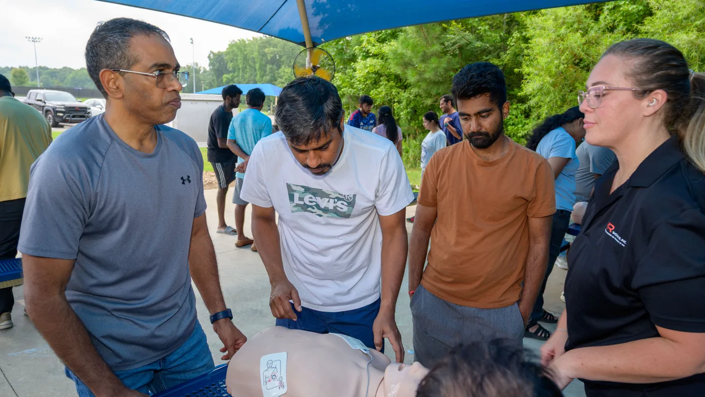 Community members practice hands-only CPR on manikins at an outdoor park table while a CPR Works instructor coaches them