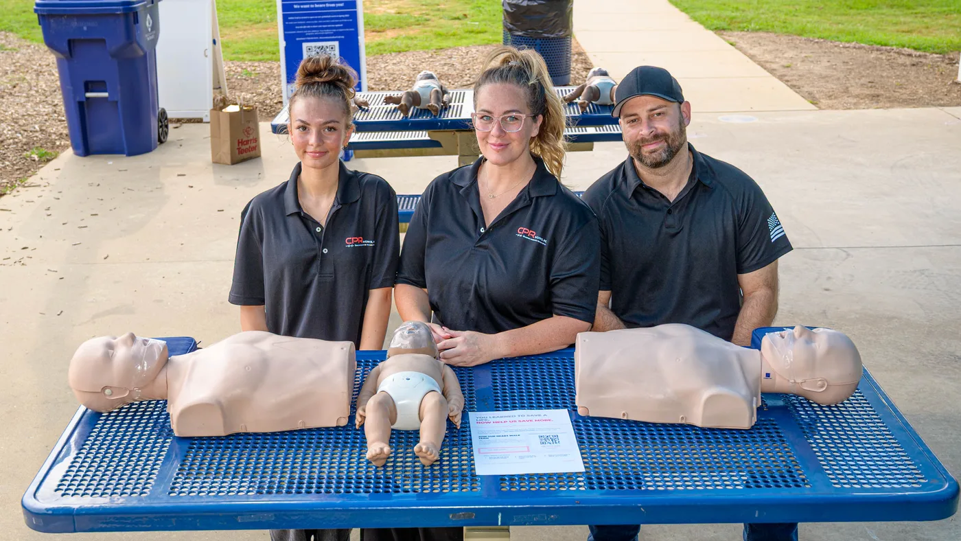 El equipo de CPR Works of Charlotte detrás de una mesa con maniquíes de entrenamiento para adultos y bebés