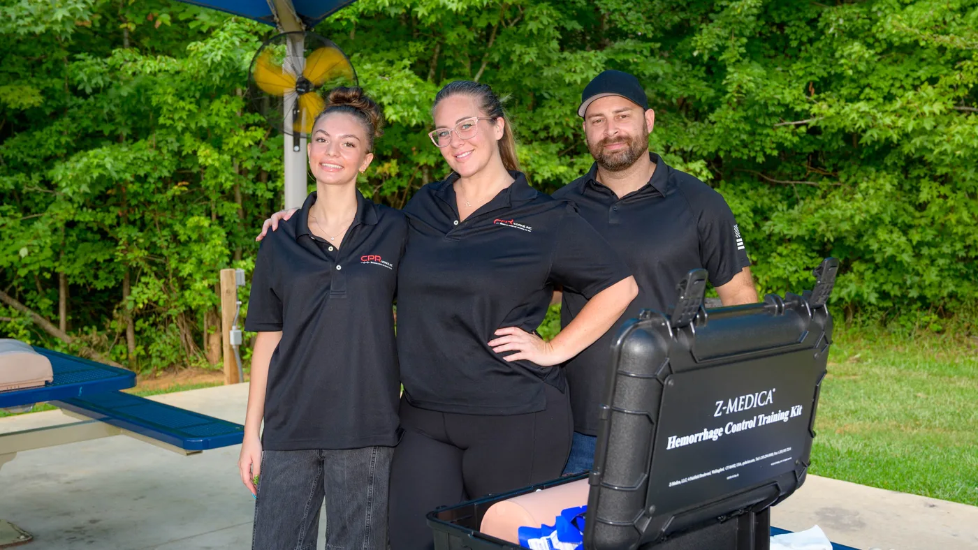 Tres integrantes del equipo de CPR Works juntos junto a un kit abierto de entrenamiento para control de hemorragias en una clase al aire libre