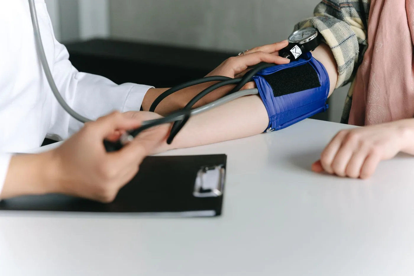 Close-up of a clinician placing a blood pressure cuff on a patient's upper arm and reading the gauge