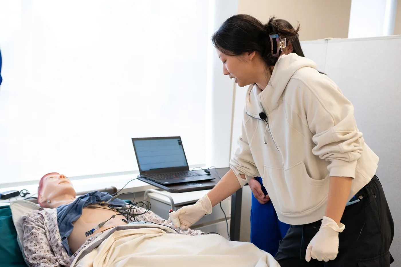A nurse educator works through a scenario on a patient simulation manikin in a skills lab, with a laptop running the case